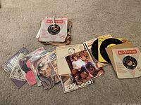 Lot of 45 RPM vinyl records scattered on carpet, showing several record sleeves with artist photos and printed designs including George Kirby and Richard Rodgers