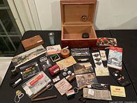 Wooden humidor box open and display of vintage fishing, boating, tools, and related small items laid out on table