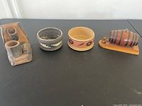 Four items: a rustic toothpick dispenser with ashtray and matchbox holder, a small round decorative bowl, a gray pottery ashtray, and a barrel-shaped ceramic container on a wooden base.