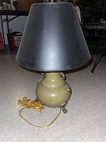 Full view of the table lamp with black shade and yellow electric cord coiled beside it, set on a floor.