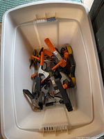 White plastic tub containing various clamps with orange, black, and yellow handles and grips