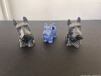 Three Yorkie figurines: two black and beige pottery dogs and one blue glass paperweight figurine on dark surface.