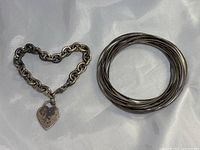 Heart charm chain bracelet and multi-bangle bracelet lying flat on a white surface, showing overall condition and design.