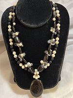 Full view of the necklace on a black velvet display showing pearls, onyx, crystals and the large pendant.