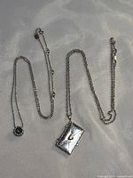 Two sterling silver chains, one with a circular blue diamond pendant, the other with an envelope pendant