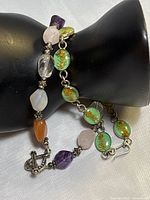 Two bracelets displayed on a black hand model showing the gemstone and flower resin designs, clasp details visible