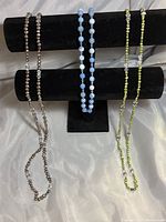 Three beaded necklaces displayed on a black T-bar stand showing their length and bead details.