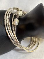 Close-up image of four diamond-cut sterling silver bangles and one sterling silver pearl bracelet on a black display hand showing texture and design of bangles and size of pearls.