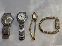 Four watches displayed side by side on fabric background: two silver-tone men's watches on left, two gold-tone ladies' watches on right.
