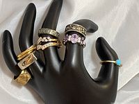 Four rings displayed on black hand stand against white drape, central overview