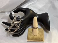 View of silver cuff bracelet with a starfish design placed on a black display hand, with the 10k gold ring on a beige ring holder in background.