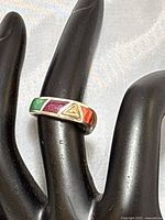 Front and side angle of the multi-gemstone inlaid ring showing purple, green, red, and orange-yellow stones with a gold triangular accent.