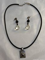 Photo showing black leather cord necklace with rectangular sterling silver pendant featuring black onyx stone, alongside matching earrings with black onyx and frosted quartz beads