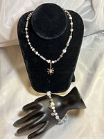 Front view of necklace displayed on a black bust, showing multi-gemstone and pearl beads with sun pendant detail. Bracelet displayed on a black hand model showing matching beads.