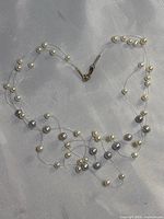 Full view of the 3-strand pearl necklace showing gray and white pearls on fine wire laid in a heart shape.
