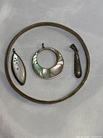 Photo of two sterling silver pendants with mother-of-pearl inlays, one alpaca pendant, and a brass bracelet arranged together.