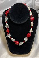Necklace displayed on black velvet stand showing the arrangement of red coral beads, white pearl clusters, and clear crystal clusters.