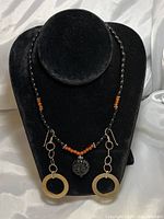 Photo of a black velvet necklace bust displaying beaded necklace with black onyx and carnelian, and a carved black jade pendant with silver circle dangling earrings on each side.