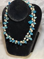 Front view of double-stranded necklace showing blue marbled beads and white pearls on black display stand.