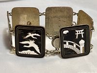 View of bracelet showing square linked panels with black and white enamel dragon and bridge scenes