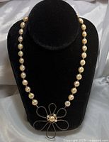Photo of 18-inch pearl necklace with silver flower pendant on black display stand, showing full length and front view of pendant and beads.