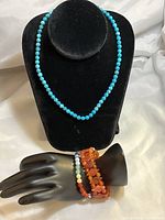 Blue turquoise round bead necklace displayed on black bust along with three gemstone bracelets on black hand display, featuring multi-gemstone, carnelian chip stone, and mixed gemstone beads.