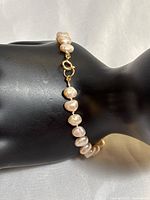 Close-up view of the bracelet clasp and pearls on a black display hand showing the gold filled clasp and creamy pearl colors.