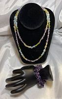 Photo shows the multi-gemstone beaded necklace displayed on a black stand and the amethyst beaded bracelet on a black hand display.