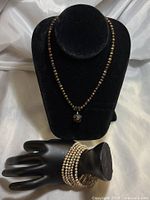 Full view of the brown chocolate pearl necklace with crystal pendant on a black display bust and the cream pearl multi-strand bracelet on black hand display.