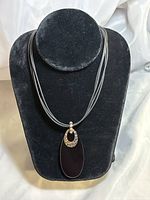 Front display of the necklace on a black velvet stand showing the black onyx pendant with silver hammered accent and four-strand leather cord.