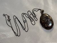 Vintage sterling silver chain extended with 1.75 inch oval locket pendant showing bird and flower engravings.