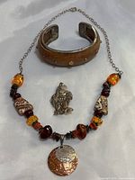 Wooden cuff bracelet with embedded sterling silver peyote bird, red coral, and quartz stones, amber necklace with mixed beads and hammered pendant, and cherub brooch all shown together