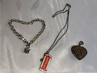 Photo of three items: sterling silver charm bracelet with box charm, sterling silver chain necklace with red-striped cylindrical pendant, and a filigree heart pendant.