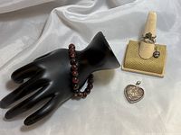 Photo showing the agate beaded bracelet on a black mannequin hand, two rings on a ring holder, a single earring with cubic zirconia mounted on ring holder, and a heart-shaped rose pendant lying beside the ring holder.