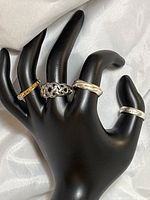 Five rings displayed on black hand jewelry holder showing gold plated diamond ring, sterling silver braided, twisted, patterned and engraved rings.