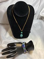 Turquoise and malachite pendant necklace displayed on black bust, blue lapis and turquoise stone bracelet shown on black hand display.