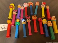 Photo showing 18 assorted Pez dispensers with character heads laid in two rows on a dark fabric surface.