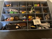 Top-down view of the open plastic organizer box showing various small collectibles, coins, and keychains in compartments. A card with number 14 placed among items.