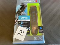 Front view of the Remington Smart Beard Trimmer 9000 in original packaging with visible front and trimmer details. Box top is torn.