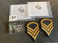 Photo showing two US Marine Corps eagle, globe, and anchor patches packaged, two black and yellow chevron rank patches, and one rectangular camouflage background patch with skull and pistol.