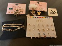 Photo shows multiple new jewelry items including earrings on branded cards and chain bracelets on a black cushion.