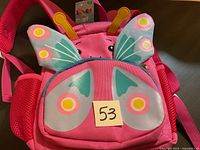 Photo showing front of small pink child's backpack with butterfly wings and yellow antennae