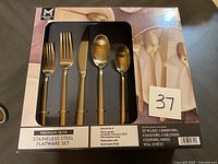 Boxed 20-piece stainless steel flatware set with gold matte finish, showing the utensils through a plastic window in the package, includes 4 dinner forks, 4 salad forks, 4 tablespoons, 4 teaspoons, and 4 knives.