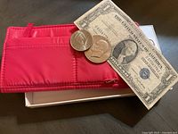 Vintage United States $1 silver certificate, Washington quarter, Kennedy half dollar, and Roosevelt dime resting on the red wallet.