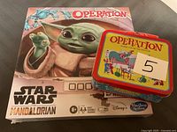 Star Wars Mandalorian Operation game box unopened with minor damage next to small vintage Operation tin
