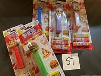 Photo showing six PEZ Treats candy dispensers in original packages with candy refills, featuring food-themed heads (pizza, hamburger, cupcake, popcorn, donut).