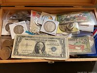 Overview of wooden box with assorted coins, paper currency, novelty notes, stamps and medals
