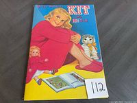 Front view of vintage Queen Holden's Kit 15.5 inch uncut paper doll booklet showing the illustrated girl in red and cat with bow.