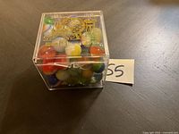 Top and front views of small clear square plastic case with gold Walt Disney World logos, filled with various colored glass marbles.