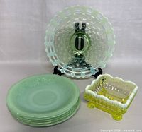 Top view showing square antique Vaseline glass candy bowl with white ruffled edge, five stacked jadeite saucers, and decorative glass plate with square pattern and cutouts.